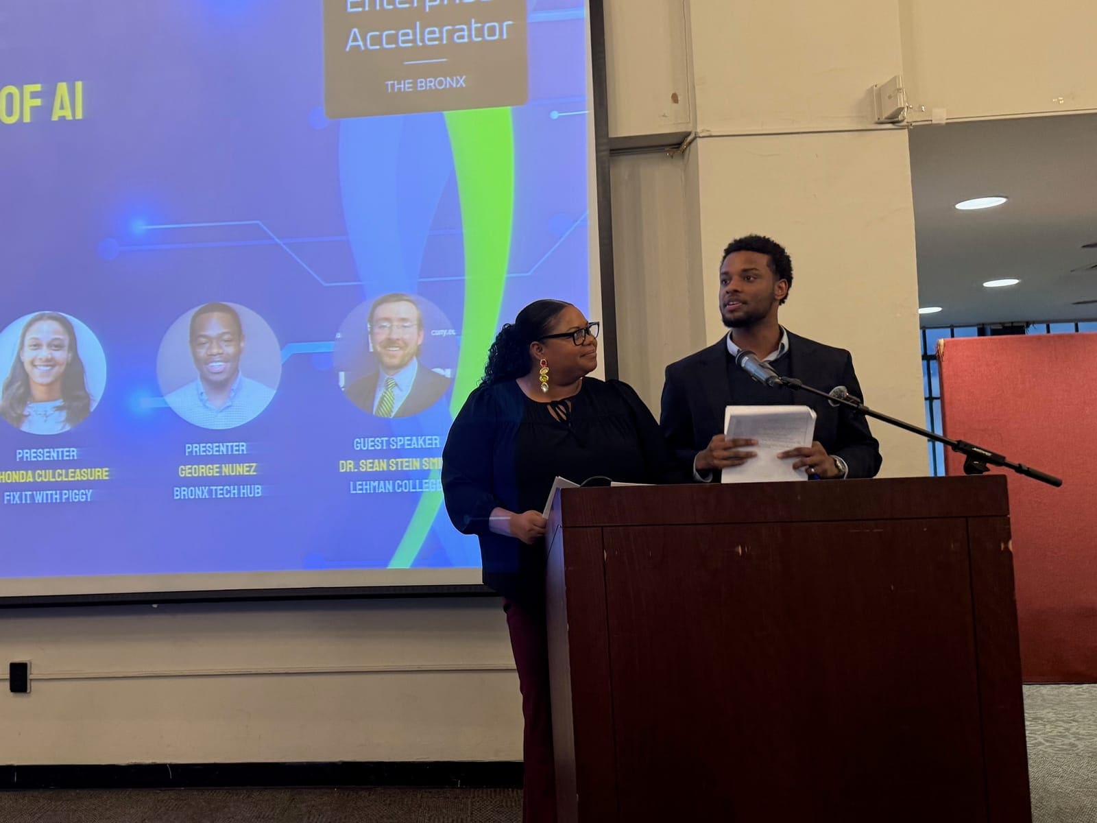 The two hosts at the podium at Bronx Brilliance at Lehman College, April 2026